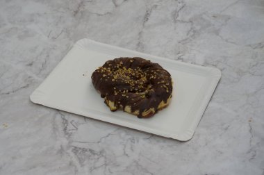 Üzerinde fındık olan çikolatalı pasta beyaz bir tabakta duruyor. Tabak mermer bir tezgahın üzerine yerleştirilmiş.