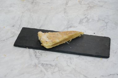 Bir dilim turta siyah bir tabağın üzerinde duruyor. Turta ikiye bölünmüş ve tepesinde bir tutam şeker var.