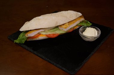 Marullu, domatesli ve tavuklu sandviç siyah bir tabakta. Sandviçin yanında küçük bir kase mayonez var.