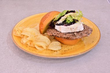 Sandviç ve patates kızartması olan bir tabak yemek. Sandviç et ve maruldan yapılır, ve patates cipsi. Tabak sarı ve yemek düzgün bir şekilde düzenlenmiş.