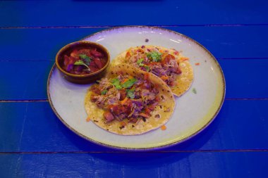 Bir tabak salsa soslu iki taco ve bir kase guacamole. Tabak mavi bir masanın üzerinde.