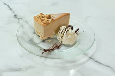 Üzerine çikolata sosu serpiştirilmiş bir dilim cheesecake. Tabak mermer bir tezgahın üzerinde.