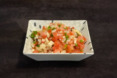 Domates ve biberli bir kase yemek. Kase beyaz ve kare. Yemekler renkli ve iştah açıcı.