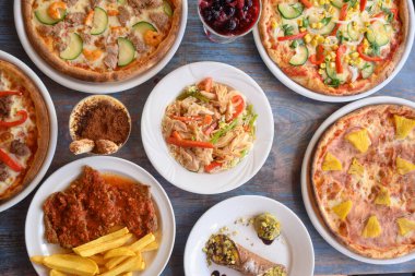 Farklı pizza çeşitleri ve diğer yiyecek maddeleriyle dolu bir masa. Olay yeri gündelik ve davetkar. Sanki aile ya da arkadaşlar bir yemeği paylaşıyor gibi.