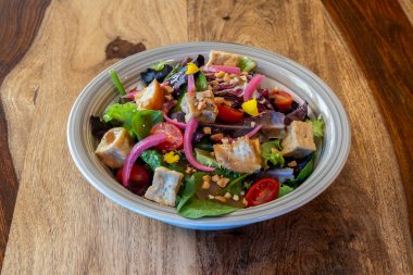 Çeşitli sebze ve fındıklı bir salata ahşap bir masada beyaz bir kasede servis edilir.