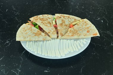 Üzerinde beyaz sos olan bir tabak yemek. Tabak siyah bir tezgahın üzerinde. Yemek bir burrito.