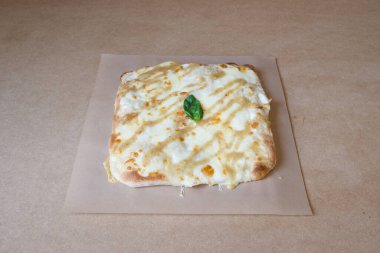 Üstünde fesleğen yaprağı olan peynirli pizza. Pizza kahverengi bir kağıt tabağın üzerinde duruyor.