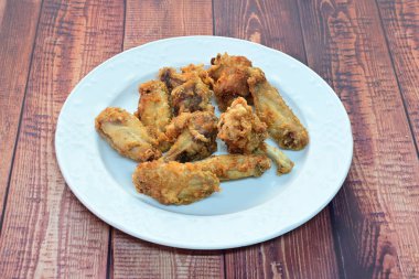 Bir tabak kızarmış tavuk kanadı ahşap bir masada duruyor. Tabak beyaz ve tavuk kanatları altın kahverengidir. Kızarmış tavuk kanatları popüler olduğu için hoşgörü ve konfor kavramı