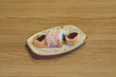 Beyaz tabağın üstünde pembe soslu suşi rulosu. Suşi rulosu ahşap bir masanın üzerinde.
