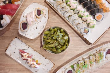 Çeşitli suşi ruloları ve diğer yemekler bir masada sergilenir. Suşi ruloları farklı şekil ve boyutlarda sıralanmıştır, bazıları daha büyük ve diğerleri daha küçüktür.