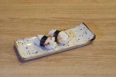 Bir tabak suşi ahşap bir masada oturur. Suşi beyaz bir tabakla yapılır ve siyah beyaz bir tasarımı vardır.