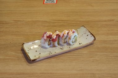 Pembe soslu suşi rulosu ve beyaz tabakta avokado. Tabak ahşap bir masanın üzerinde.