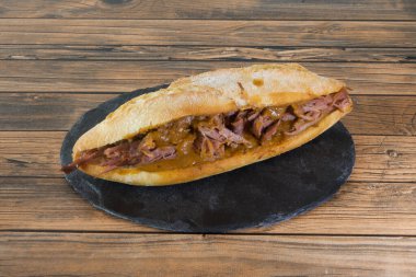Siyah tabakta et ve et soslu bir sandviç. Sandviç ahşap bir masanın üzerinde. Sandviç ikiye bölünür ve siyah bir tabağa konur.