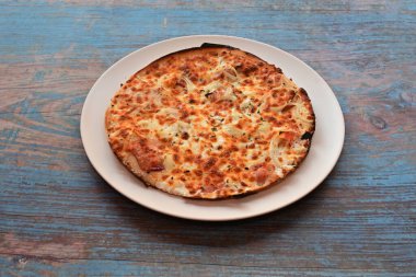 Beyaz tabakta peynirli ve jambonlu bir pizza. Pizza ahşap bir masada oturuyor.