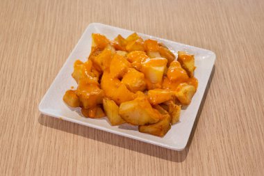 Kremalı soslu bir tabak patates dilimi. Tabak beyaz, patatesler turuncu.