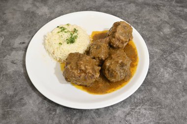 Üstünde sos olan bir tabak köfte ve pilav. Tabak beyaz ve köfteler kahverengi.