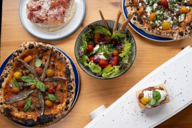 İçinde pizza, salata ve tatlı gibi çeşitli yiyeceklerin olduğu bir masa. Masa yemek için hazır, yemek de lezzetli ve davetkar görünüyor.