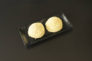 Siyah tabakta iki küçük sarı hamur işi. Pastalar yuvarlak ve hamurdan yapılmış gibi görünüyorlar.