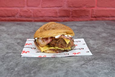 Kırmızı ve beyaz peçeteli pastırmalı ve peynirli bir hamburger. Hamburger masanın üstünde.