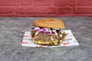 Kırmızı zemin üzerinde et ve soğan olan bir sandviç. Sandviç kağıt peçetenin üzerinde.