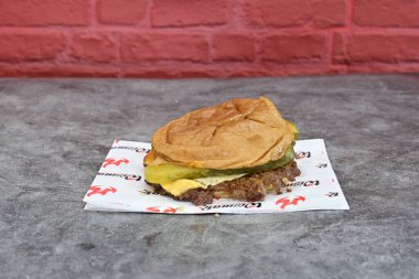 Kağıt peçeteye turşulu ve peynirli bir hamburger. Hamburger masanın üstünde.