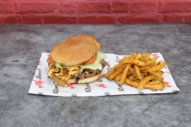 Kırmızı beyaz peçetenin üzerinde hamburger ve patates kızartması var. Hamburger marul ve domatesle kaplı.
