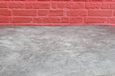 Gri bir masa kırmızı tuğla bir duvarın önünde oturur. Masa boş ve duvar da kırmızının koyu tonu. Masa ve duvar arasındaki zıtlık, sahnede derinlik ve ilgi hissi yaratıyor.