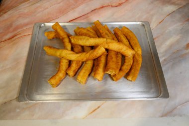 Bir tepsi kızarmış çörek mermer tezgahın üzerinde duruyor. Çörekler altın kahverengidir ve düzgün bir sıra halinde dizilmiştir. Zevk ve hoşgörü kavramı, lezzetli ikramlar tatmaya hazır.