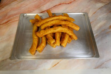 Bir tepsi kızarmış çörek mermer tezgahın üzerinde duruyor. Çörekler altın kahverengidir ve taze yapılmış gibi görünüyor. Tepsi gümüş ve dikdörtgen şeklinde. Sahne sıcak ve davetkar.