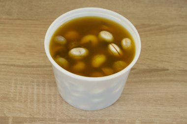 İçinde kahverengi sıvı olan beyaz bir plastik kap. Konteynır fındık ve fasulye ile dolu. Sıvı kahverengi ve kalın bir kıvama sahip.