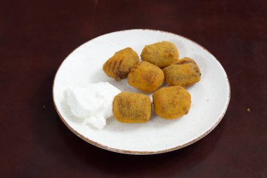 Üstünde beyaz sos olan bir tabak kızarmış yemek. Yemek küçük ve yuvarlak. Tabakta altı parça yiyecek var.