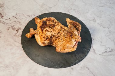 Bütün bir tavuk siyah bir tabağın üzerinde oturuyor. Tavuk pişti ve çok baharatlı.