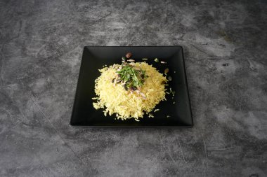 Üstünde fındık ve otlar olan bir tabak pirinç. Tabak siyah ve pirinç sarıdır.