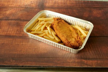 Bir parça kızarmış tavuk bir tepsi patates kızartmasının üzerinde oturuyor. Tavuk kahverengidir, patates kızartması da altın sarısıdır.