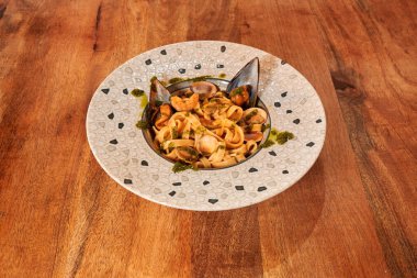 Bir tabak köfteli ve yeşil soslu makarna. Tabak ahşap bir masanın üzerinde. Makarna tabağın ortasında ve köfteler etrafa saçılmış.