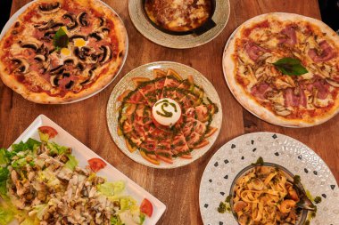 Bir masa dolusu pizza ve salata. Dört pizza ve üç salata var.