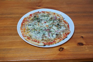 Beyaz tabakta peynirli ve soğanlı bir pizza. Tabak ahşap bir masanın üzerinde. Pizza dilimlenmiş.