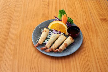 Bir tabak portakal dilimleri ve soslu karides köftesi. Tabak ahşap bir masanın üzerinde.