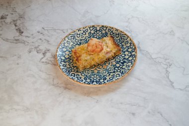 Mavi bir tabakta bir parça yiyecek var. Tabak mermer tezgahın üzerinde. Yemek bir dilim pizzadır.