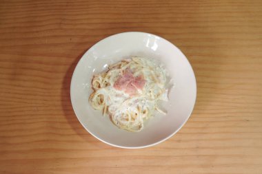 Üstünde peynir ve et olan bir tabak makarna. Tabak beyaz, makarna beyaz.