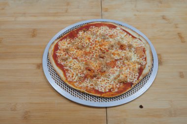 Peynirli ve etli bir pizza metal bir tavada durur. Tava ahşap bir masanın üzerinde.