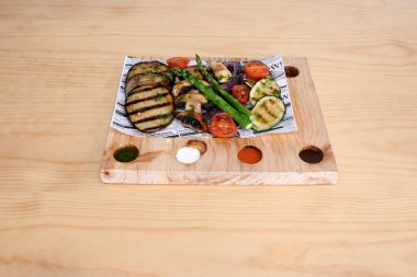 Tahtada bir tabak sebze ve et. Sebzeler arasında kuşkonmaz, kabak ve domates var.