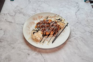 Çikolata soslu bir tatlı ve beyaz tabağın üstünde krema. Tabak mermer tezgahın üzerinde.