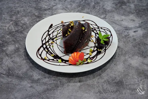 Çikolata soslu bir tatlı ve beyaz tabakta çilek. Tatlı, üzerine çikolata sosu serpiştirilmiş bir pasta.
