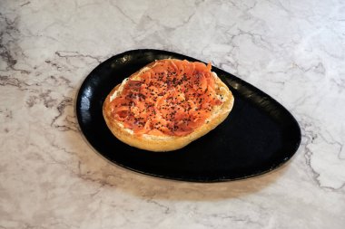 Somon ve susam tohumlu bir parça ekmek. Siyah bir tabakta.