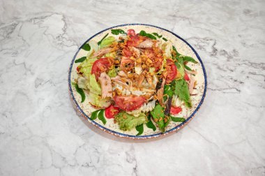 Salata, marul, domates ve tavuklu beyaz tabak. Tabak mermer tezgahın üzerinde.