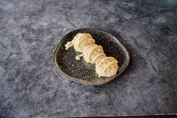 Üzerinde beyaz sos olan siyah bir tabak. Sos yemeğin üzerine serpilmiş, yani bir tatlı. Tabak gri bir yüzeye yerleştirilmiş, muhtemelen bir tezgah ya da masa.