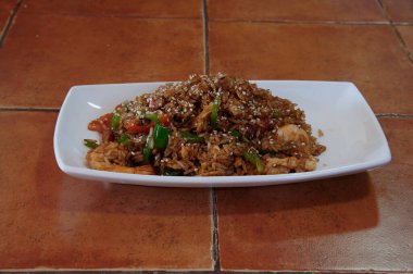 Pirinç ve sebzeli bir tabak yemek. Tabak beyaz ve dikdörtgen. Yemekler kahverengi ve çok baharatlı.