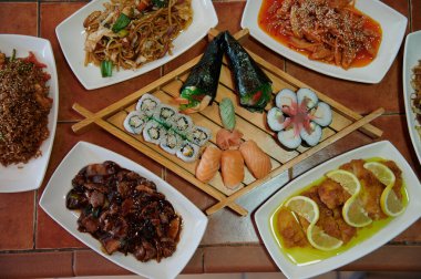 Suşi, tavuk ve limon da dahil olmak üzere bir sürü farklı yemek çeşidi olan bir masa. Masada tabaklar ve kaseler de var.