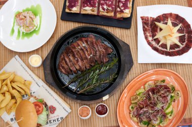 İçinde hamburger, sandviç ve salata da olan çeşitli yiyecekler olan bir masa. Ayrıca et ve sebze tabakları da var.